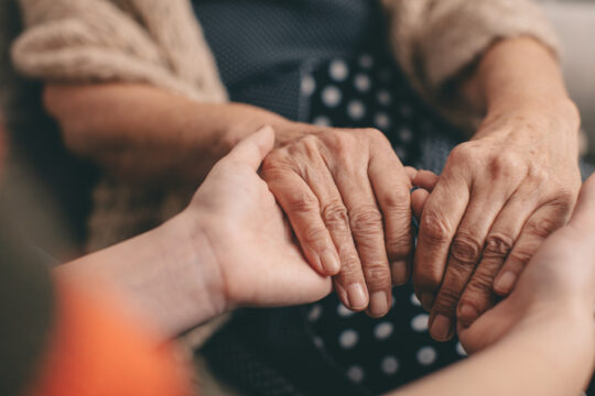 Die Hände einer Seniorin und einer Betreuerin halten einander